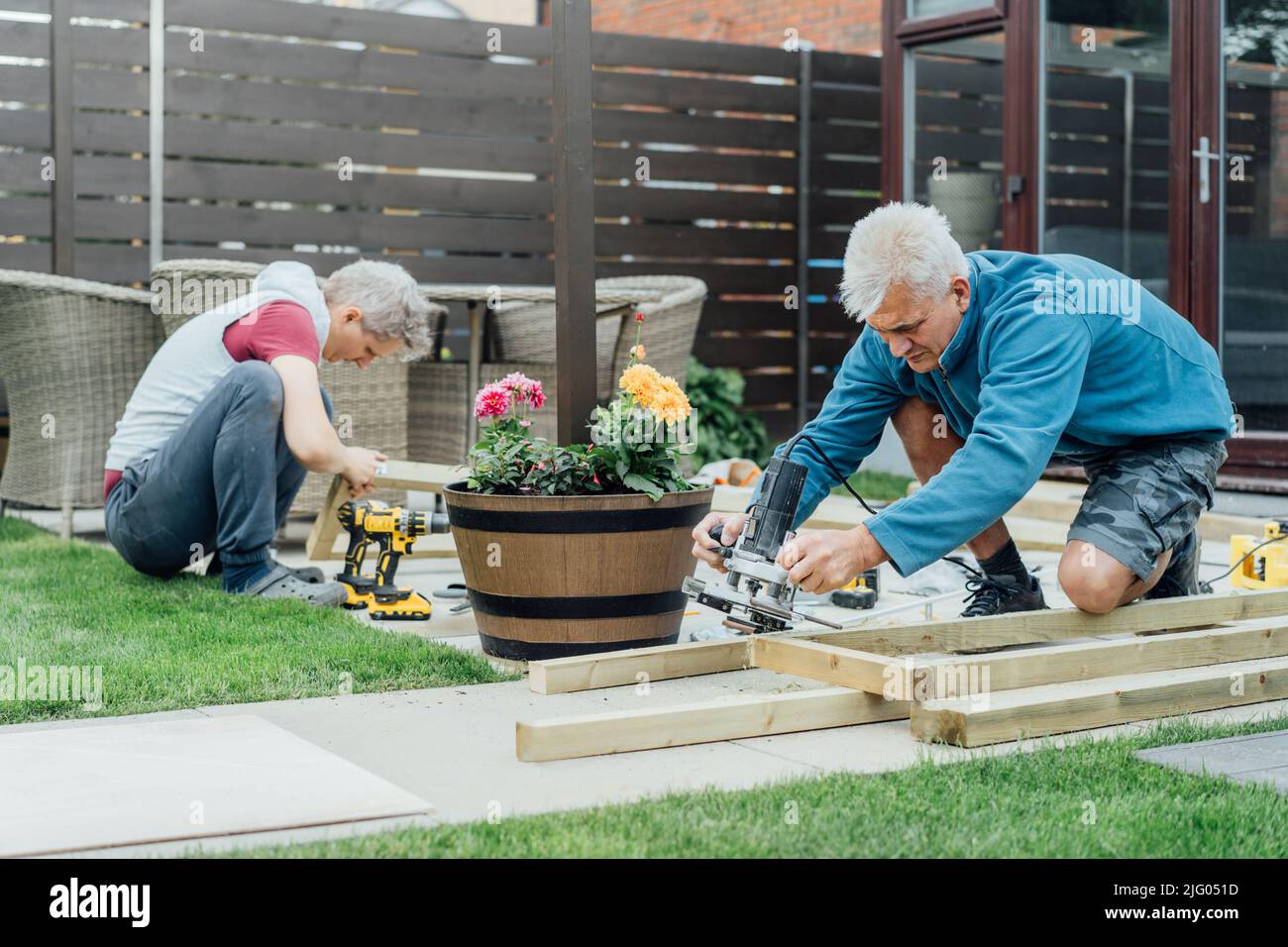 Carpentiere adulto figlio e padre che lavorano insieme, maneggiano legno di legno nel giardino. Patio in costruzione da soli. Fai da te. Ristrutturazione casa Foto Stock