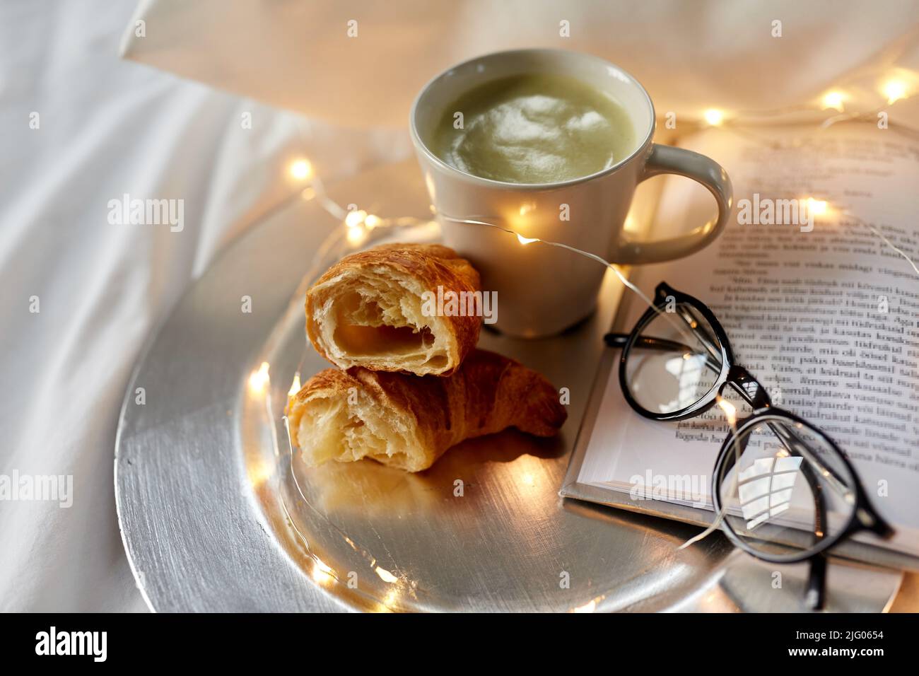 croissant, tè matcha, libro e bicchieri a letto Foto Stock