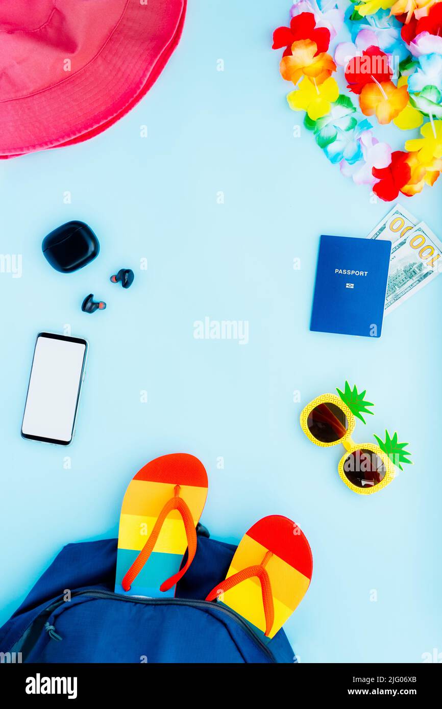 Vista dall'alto concetto di vacanza estiva con tutte le cose di viaggio necessarie. Zaino, cappello da secchio, occhiali da sole divertenti, infradito, passaporto biometrico, contanti, telefono Foto Stock