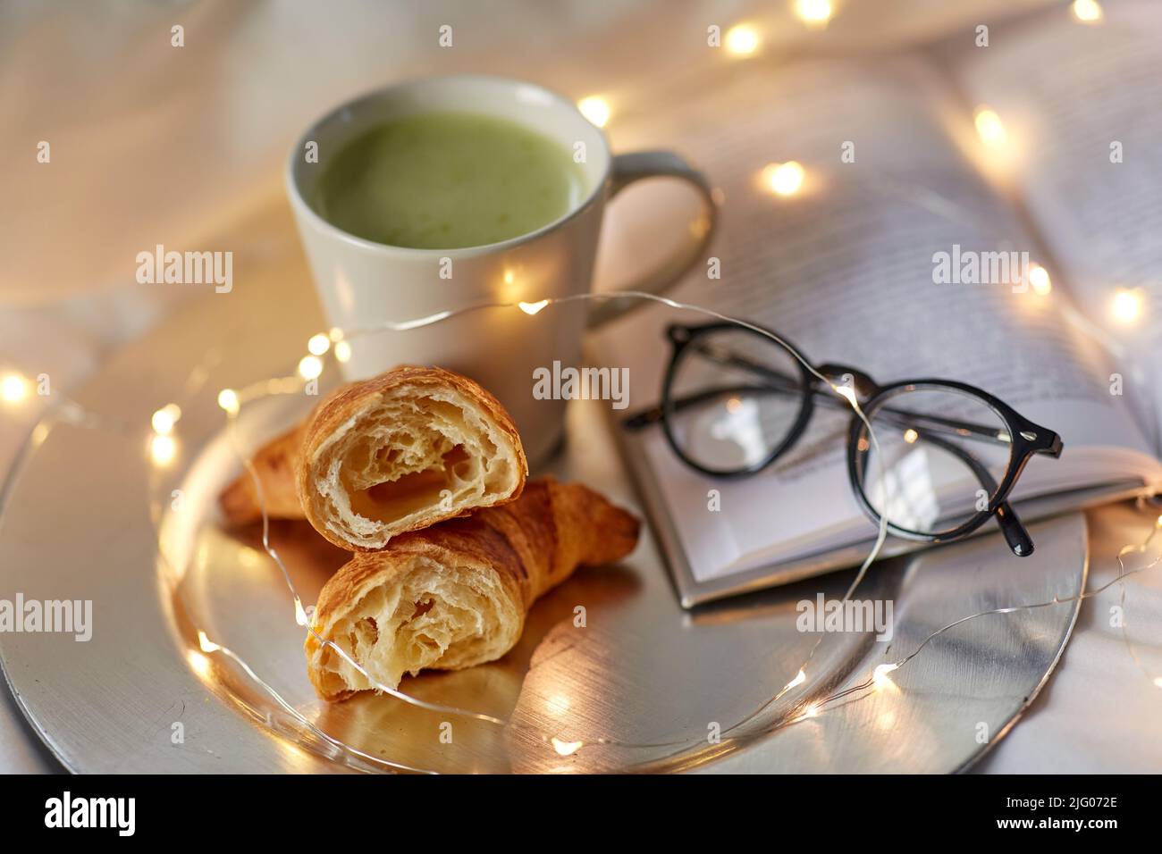 croissant, tè matcha, libro e bicchieri a letto Foto Stock