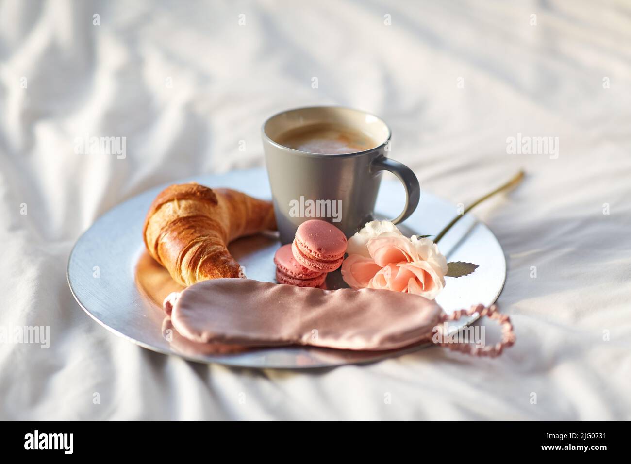 croissant, caffè e maschera per gli occhi a letto Foto Stock