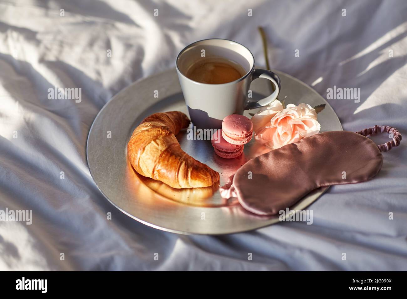 croissant, caffè e maschera per gli occhi a letto Foto Stock