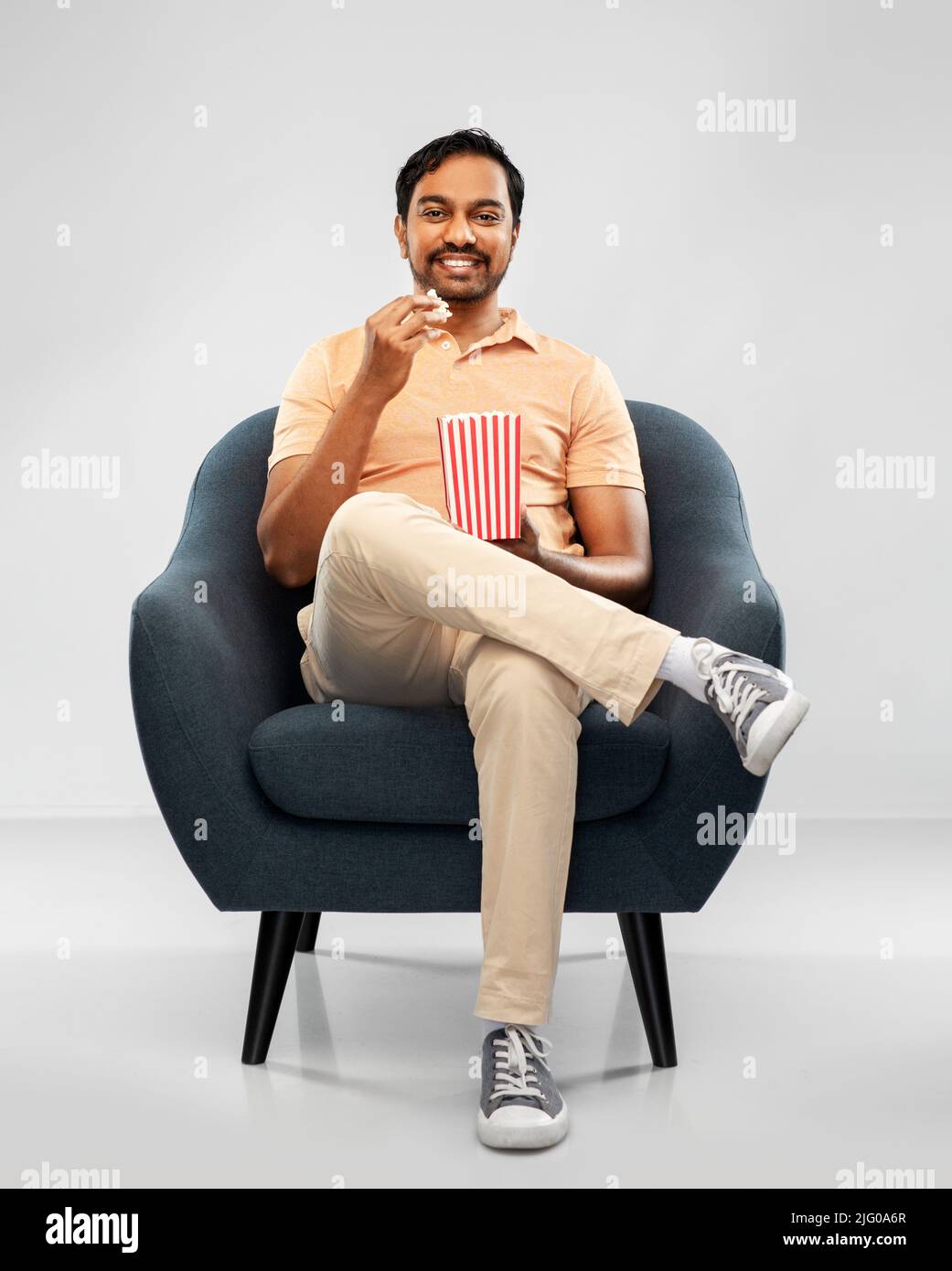 felice uomo indiano sorridente che mangia popcorn in sedia Foto Stock