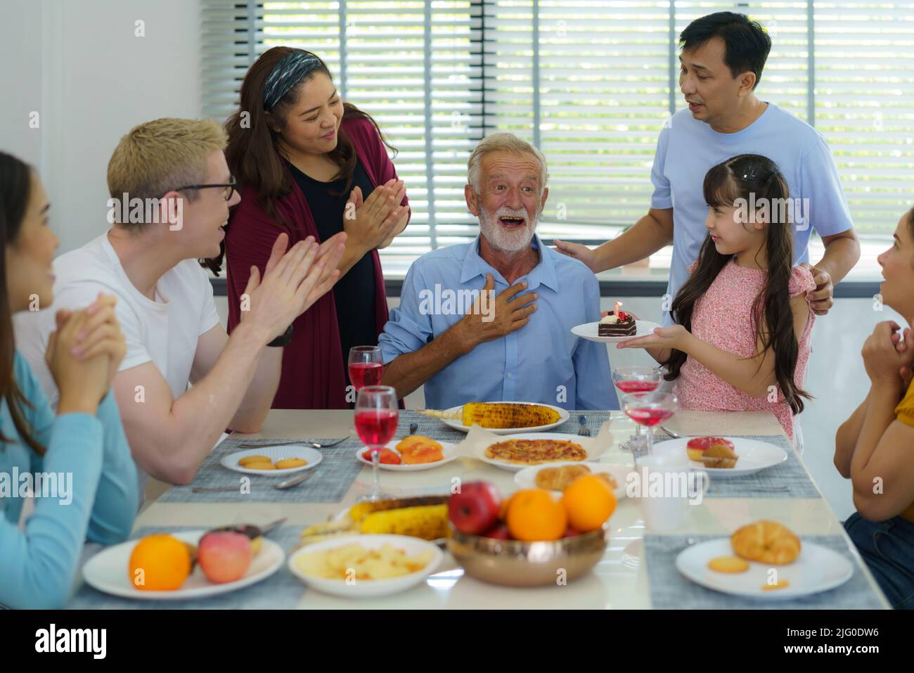 Buona multietnia e famiglia multigenerazione che festeggia il compleanno dei nonni nel soggiorno di casa. Foto Stock