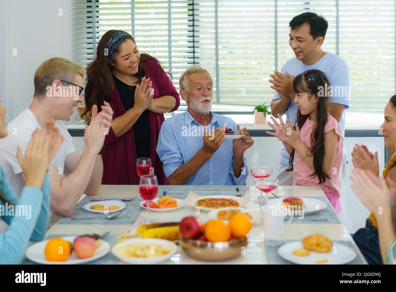 Buona multietnia e famiglia multigenerazione che festeggia il compleanno dei nonni nel soggiorno di casa. Foto Stock