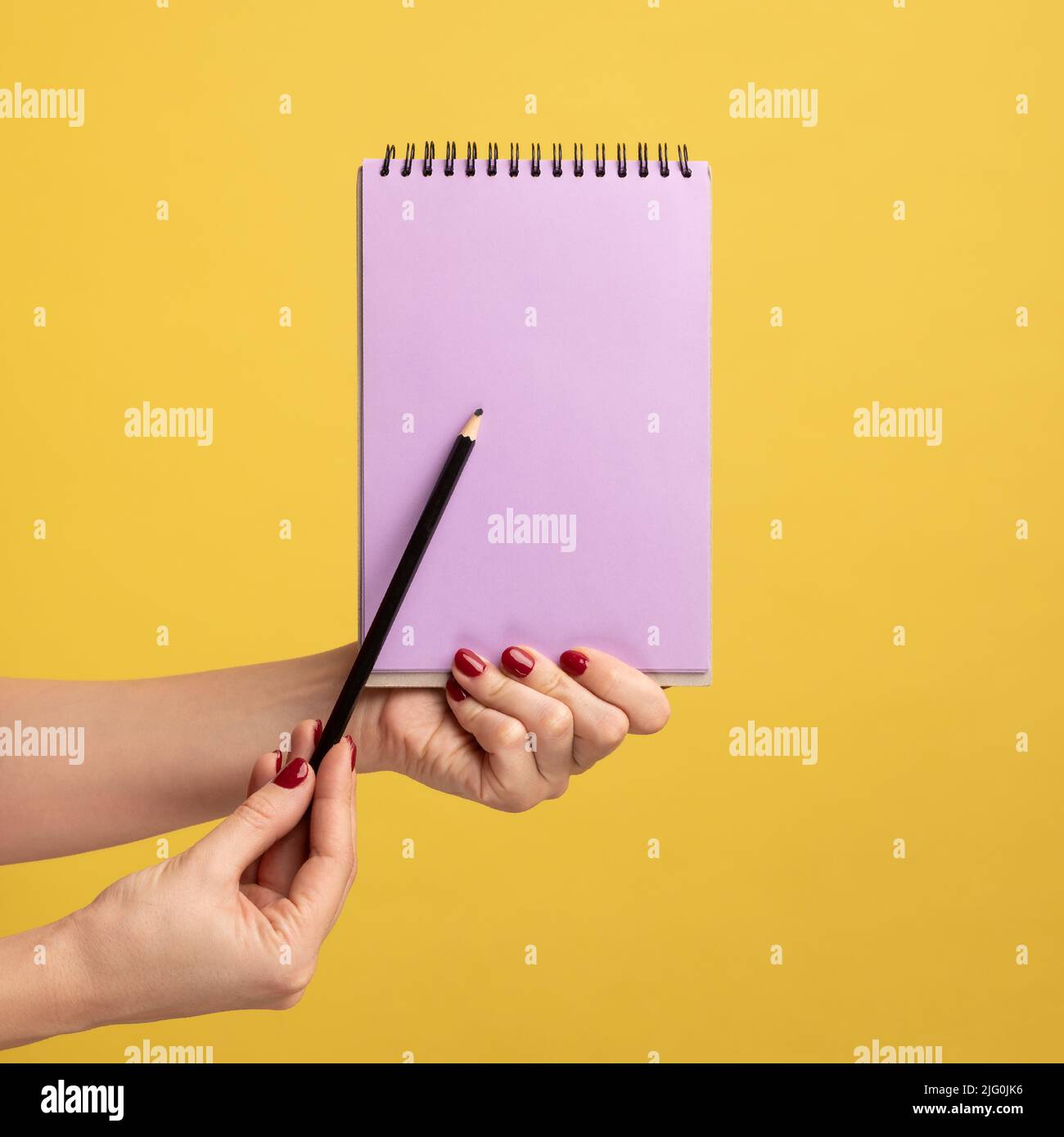Profilo vista laterale primo piano della mano donna tenendo in mano il blocco note viola e mostrando carta vuota con penna o matita. Studio interno girato isolato su sfondo giallo. Foto Stock