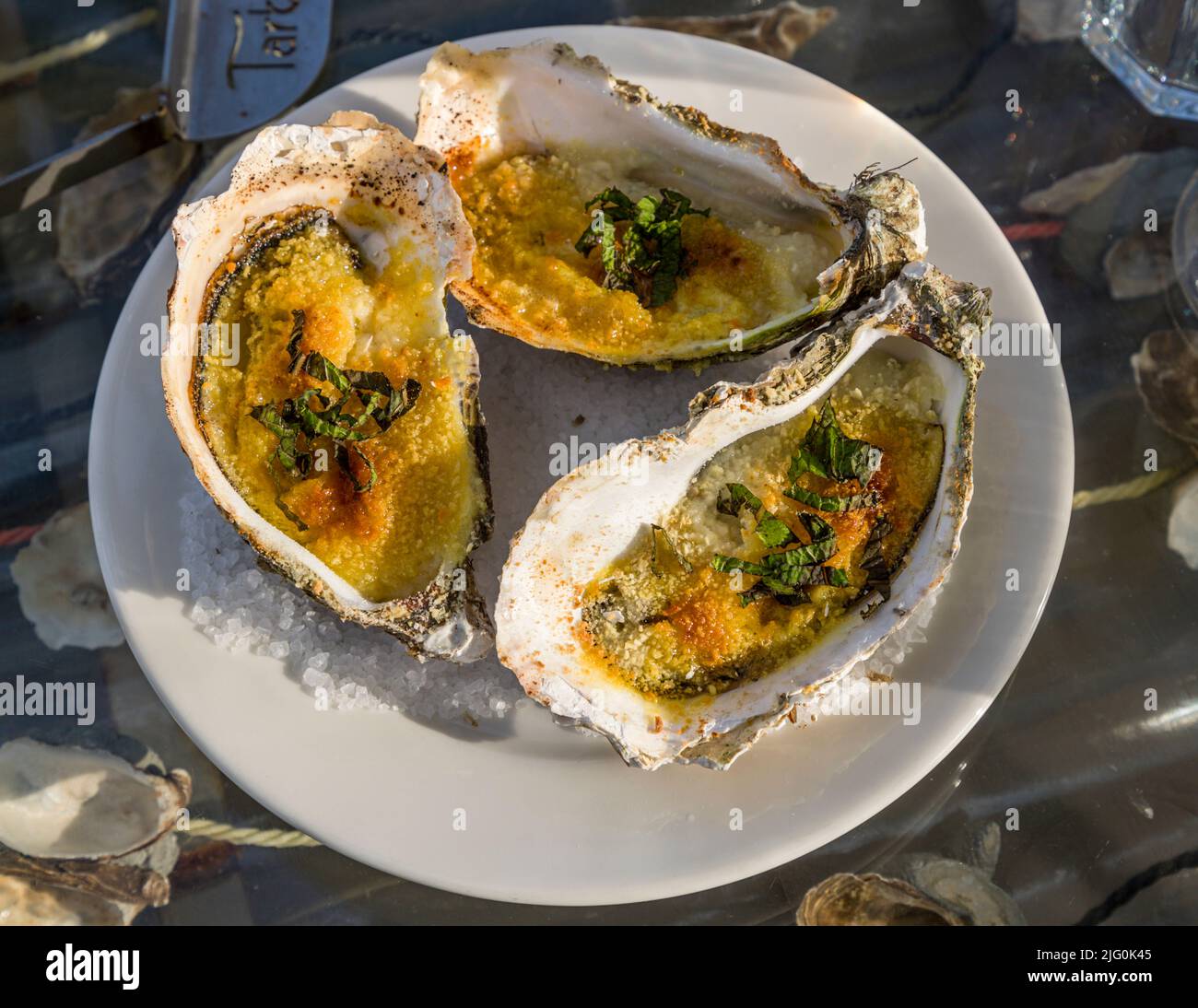 Tre ostriche gratinate ricoperte di pangrattato, menta, olio di verbena, scorza di limone e arancia sono disposte su un piatto nel padiglione balneare Le St Pierre Tarbouriech a Loupian, Hérault, Francia. Foto Stock