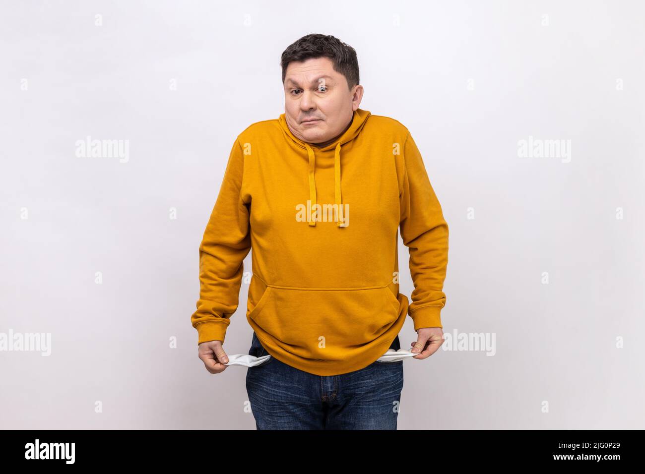 Non ho più soldi. Ritratto di triste uomo in bancarotta in piedi e mostrando la sua tasca vuota e guardando la macchina fotografica, indossando una felpa con cappuccio in stile urbano. Studio interno girato isolato su sfondo bianco. Foto Stock