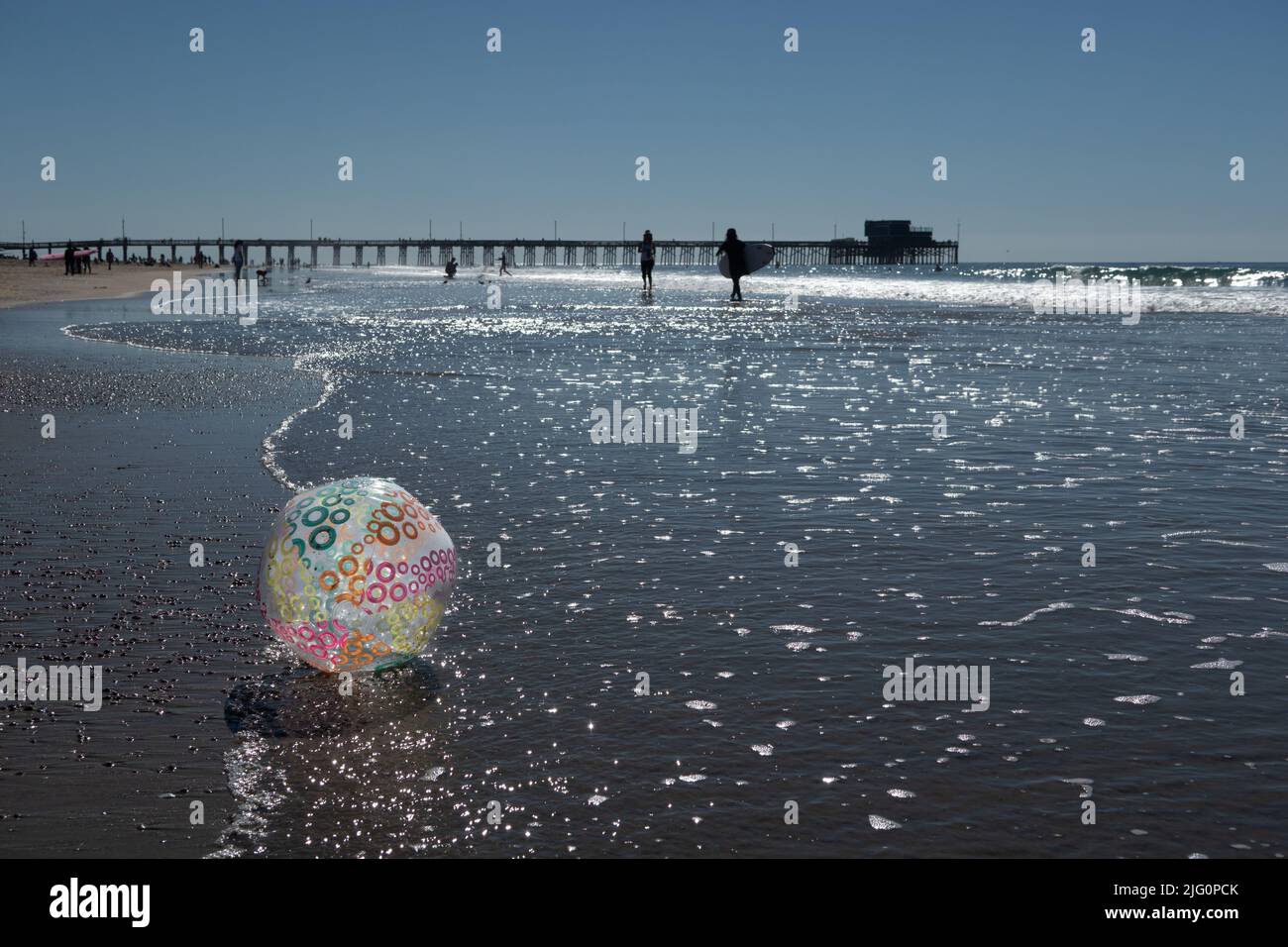 Grande pallone da spiaggia gonfiabile in primo piano del molo di newport Beach con surfisti che camminano lungo la spiaggia Foto Stock