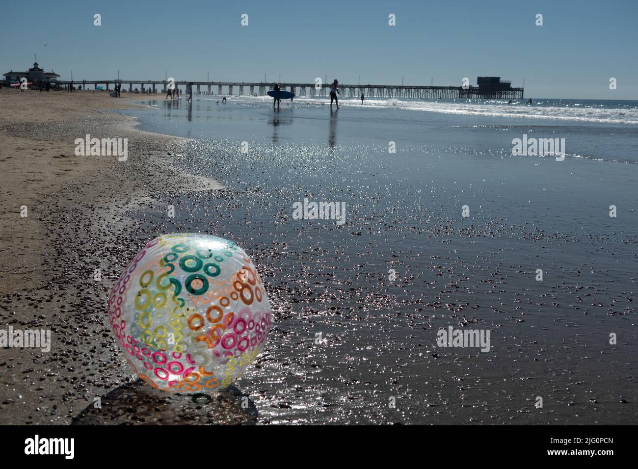 Grande pallone da spiaggia gonfiabile in primo piano del molo di Newport Beach con surfisti che camminano lungo la spiaggia Foto Stock