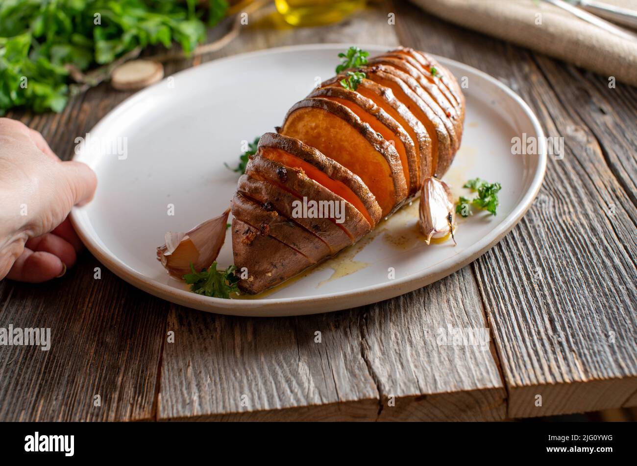 Contorno di patate sano con una patata dolce al forno. Cotto con aglio, erbe e olio d'oliva. Servito su un piatto su un tavolo di legno con spazio per la copia Foto Stock