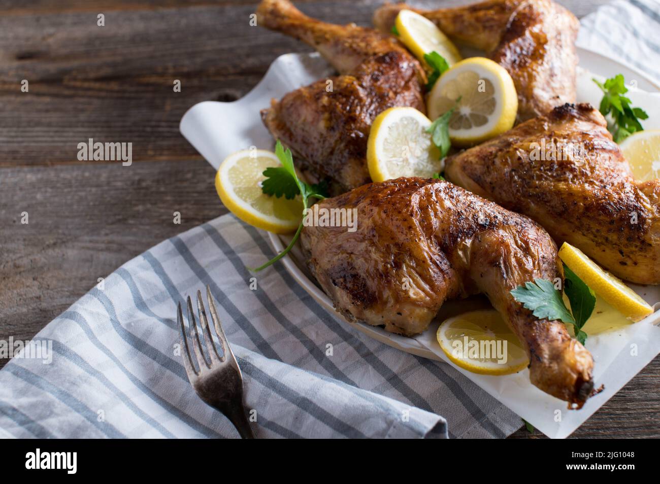 Cosce di pollo al forno con limone affettato su un piatto isolato su tavola di legno con spazio copia Foto Stock