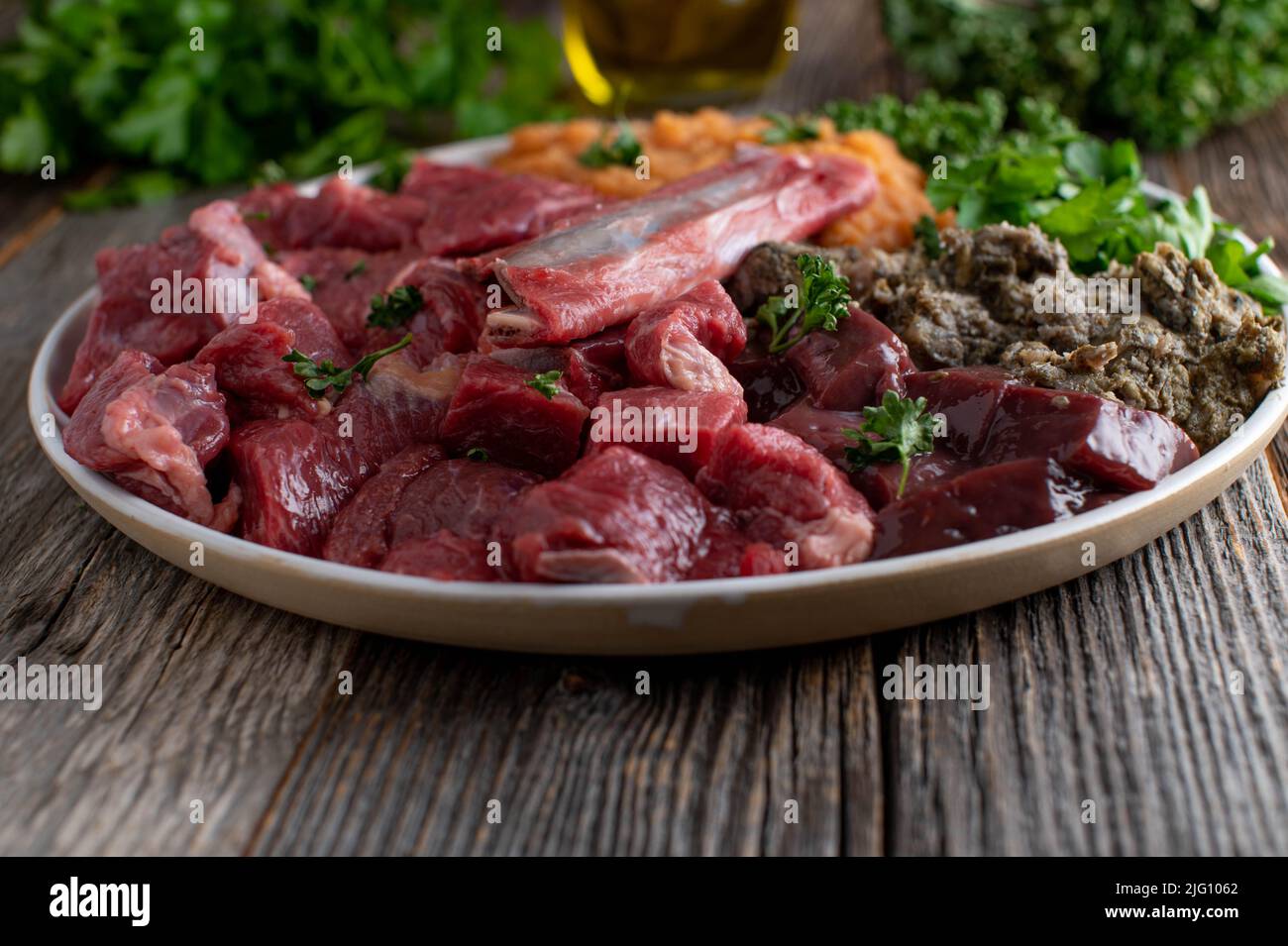 Alimentazione di carne cruda per cani. Un piatto con carne fresca muscolare, ossa, rumine, frattaglie, verdure ed erbe Foto Stock