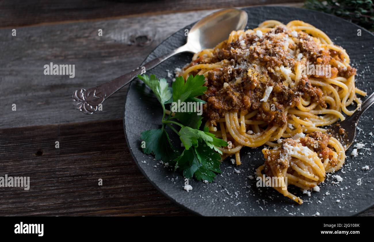 Spaghetthi bolognese su un piatto scuro su tavola di legno Foto Stock