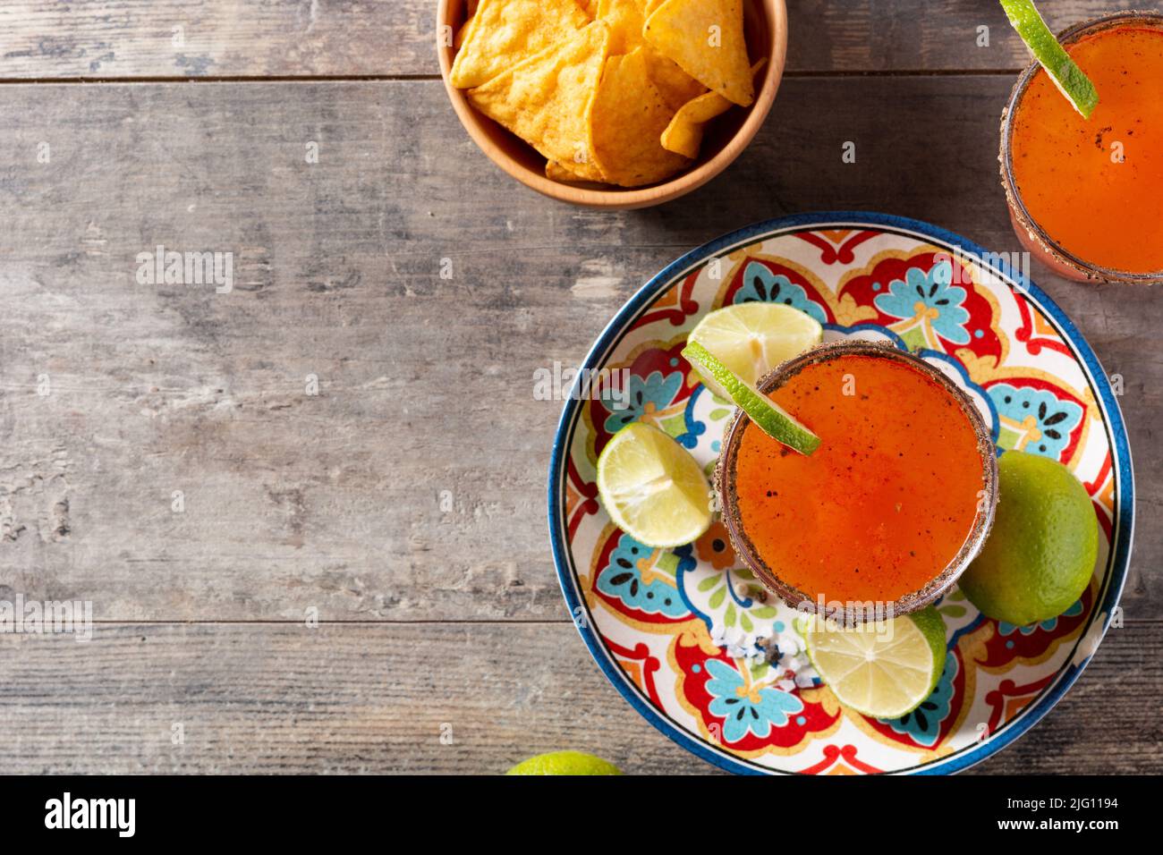 Cocktail michelada fatto in casa con birra, succo di lime, salsa calda, bordo salato e succo di pomodoro su tavola di legno Foto Stock