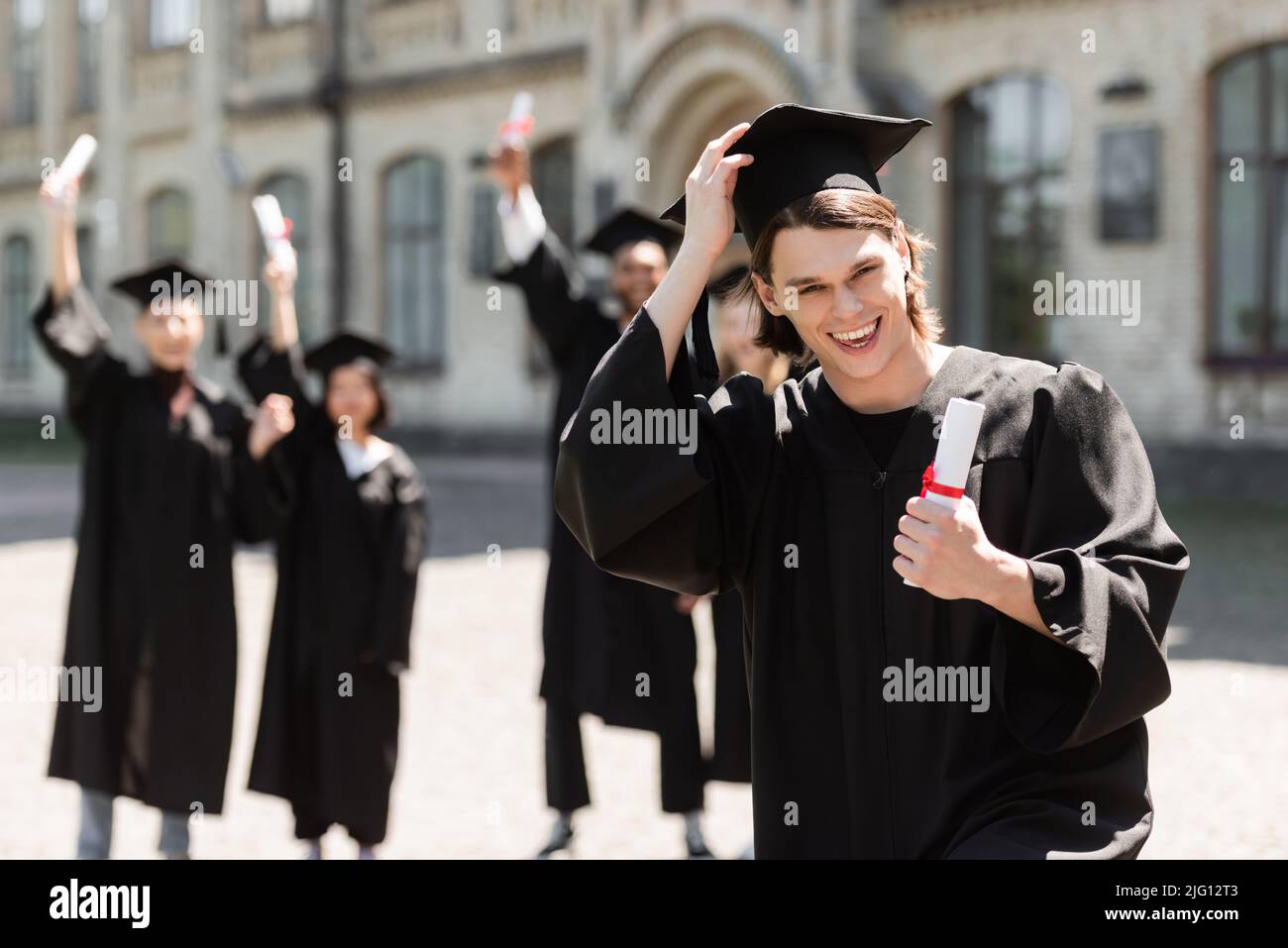 Bachelor sorridente che tiene il cappello e il diploma all'aperto Foto Stock