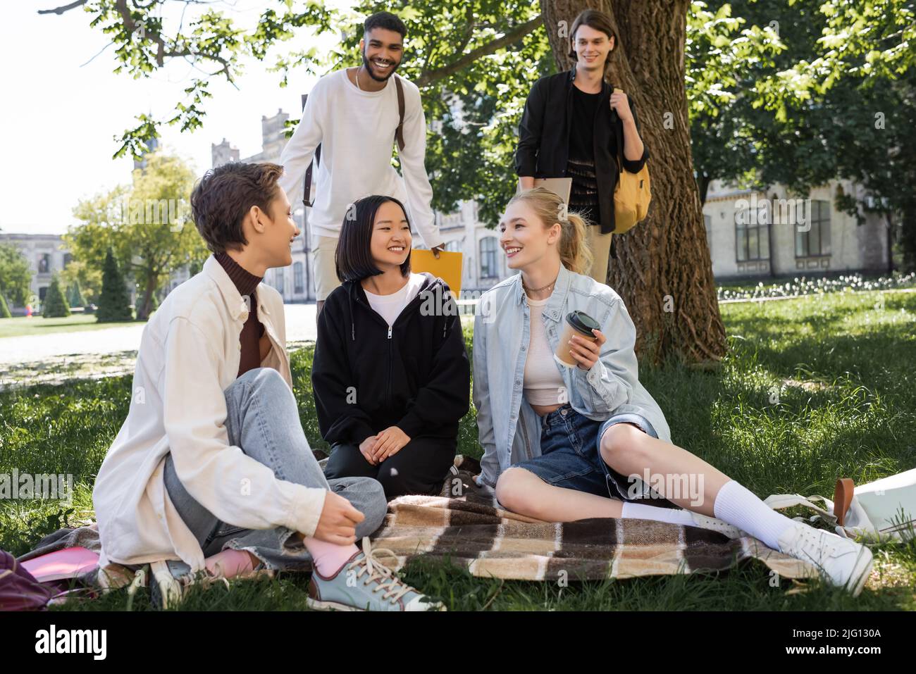 Sorridenti studenti multietnici che parlano vicino ad amici in coperta nel parco Foto Stock