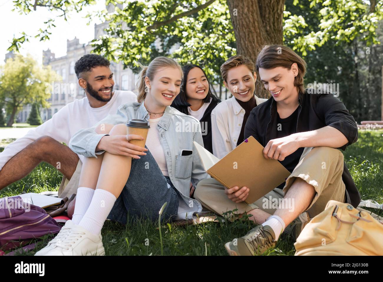 Sorridenti studenti multiculturali che guardano amici con taccuino in erba nel parco Foto Stock