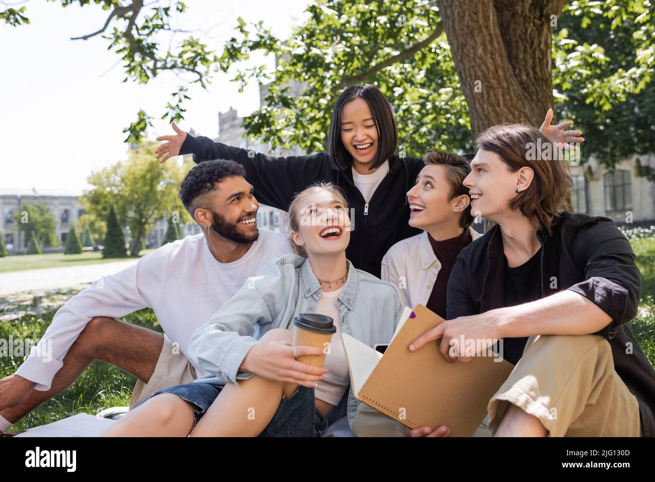 Eccitato studente asiatico guardando allegri amici interrazziali in erba nel parco Foto Stock