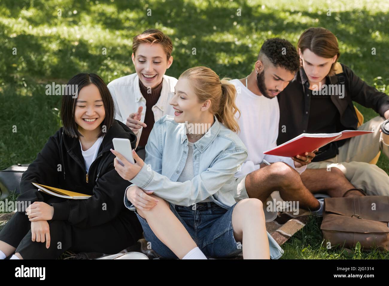 Positivo studente che tiene smartphone vicino a amici multietnici sul prato all'aperto Foto Stock