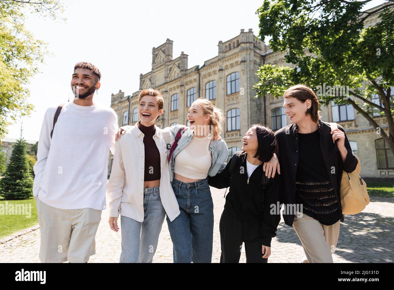 Gruppo di studenti multiculturali sorridenti che si abbraccia mentre si cammina vicino all'università all'aperto Foto Stock