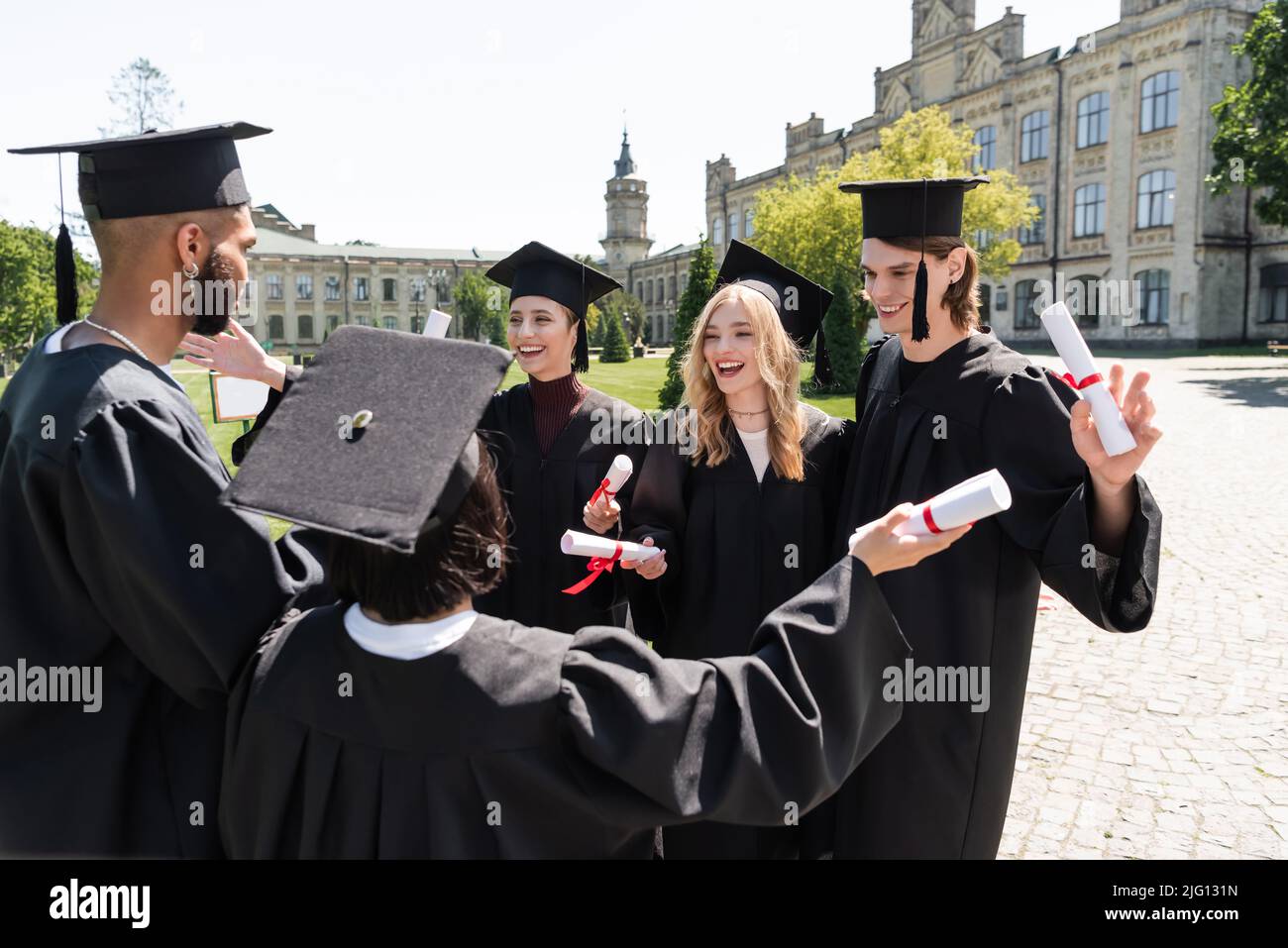 Bachelor multietnici positivi in berretti e camici che detengono diplomi nel parco Foto Stock