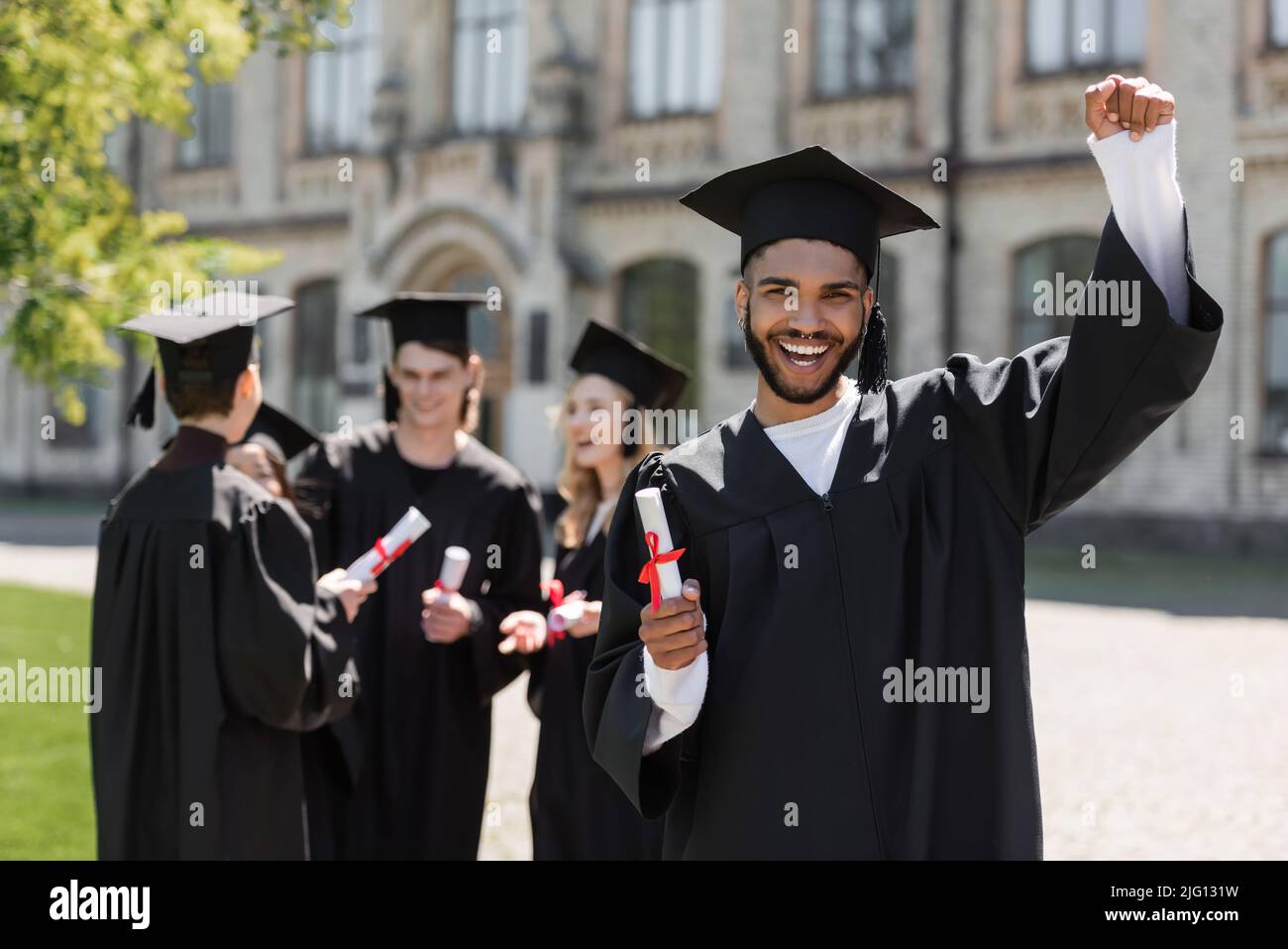 Eccitati bachelor afroamericano che tengono il diploma vicino agli amici nel parco Foto Stock