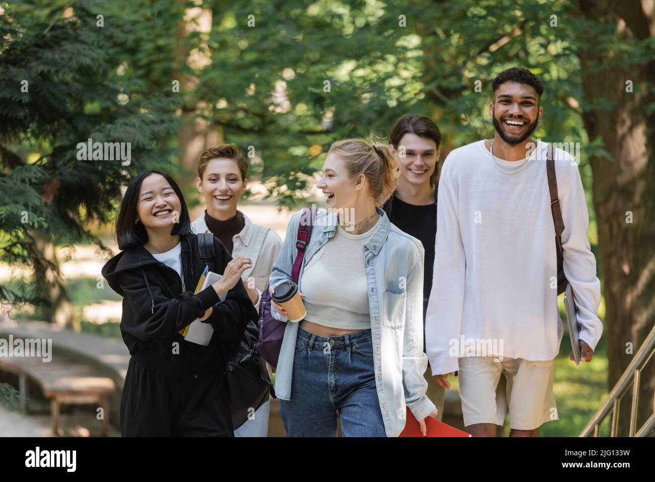Sorridente studente asiatico a piedi vicino a amici multiculturali nel parco estivo Foto Stock