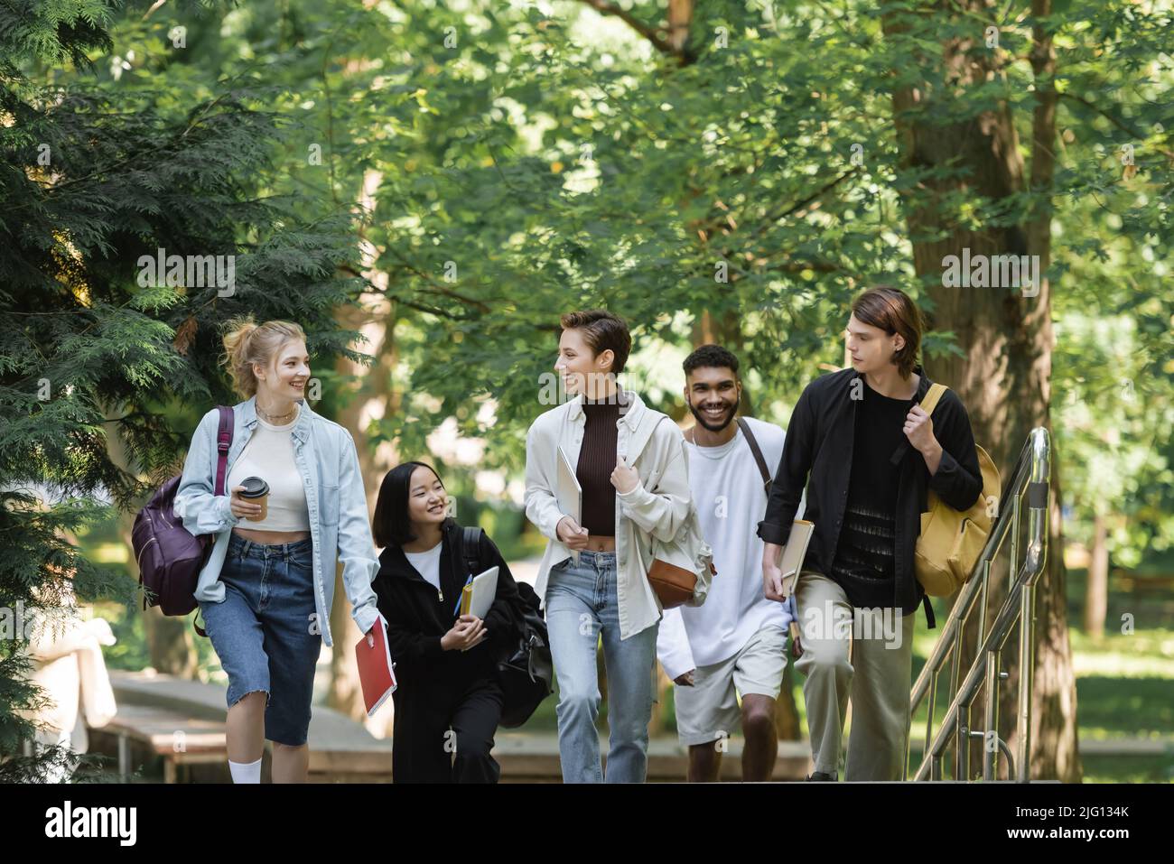 Studenti allegri con zaini che camminano vicino a amici multietnici nel parco Foto Stock