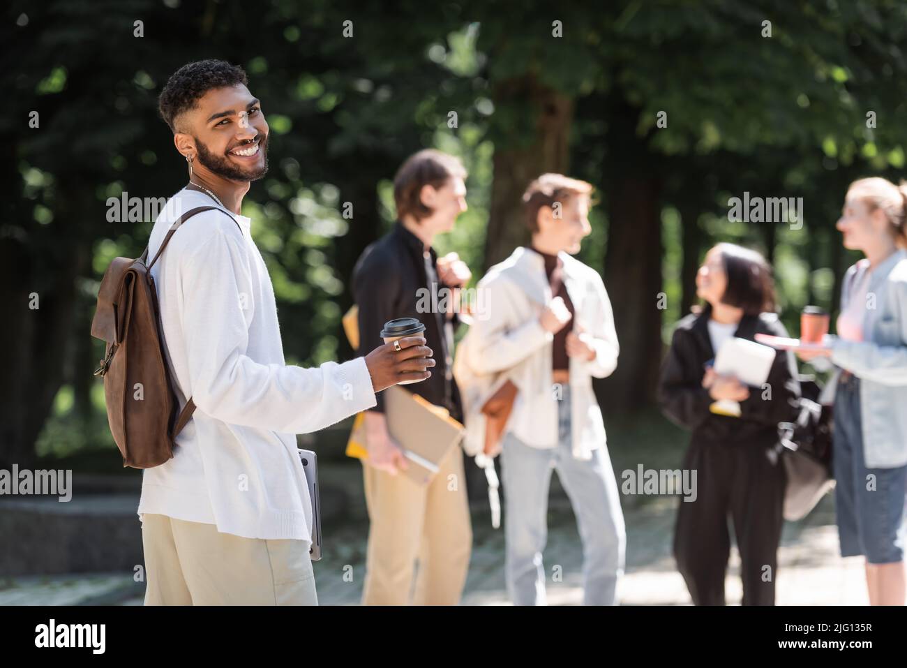 Sorridendo studente afroamericano che tiene il caffè per andare vicino a blurred amici nel parco Foto Stock