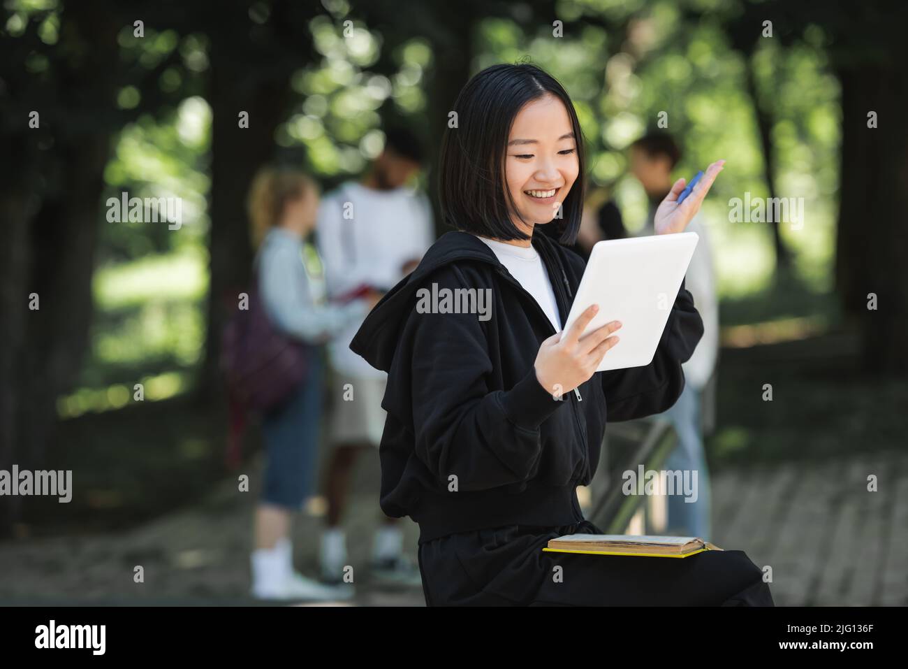 Studente asiatico positivo che ha una videochiamata sul tablet digitale nel parco Foto Stock