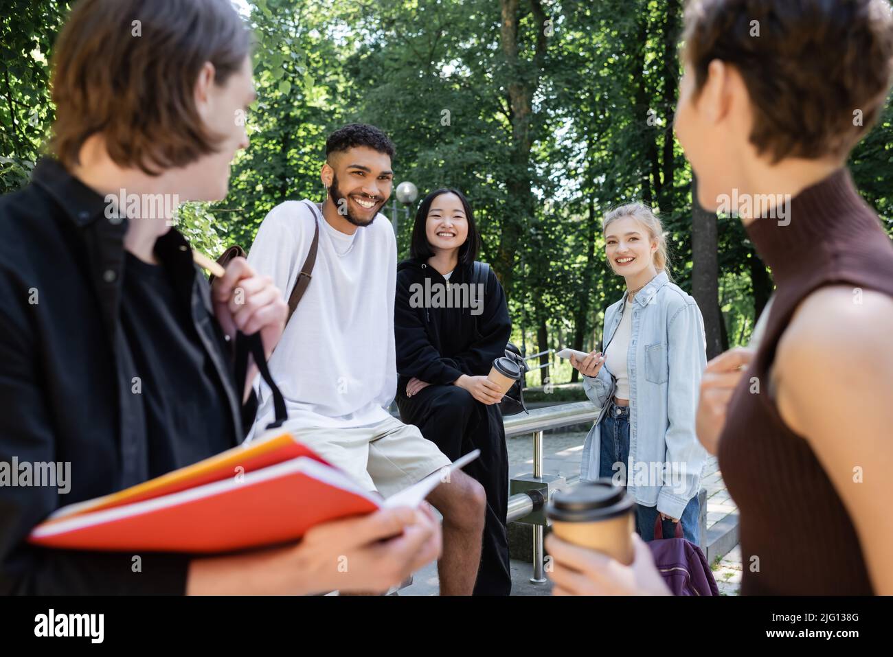 Allegri studenti multiculturali con smartphone e drink da asporto guardando gli amici sfocati nel parco Foto Stock