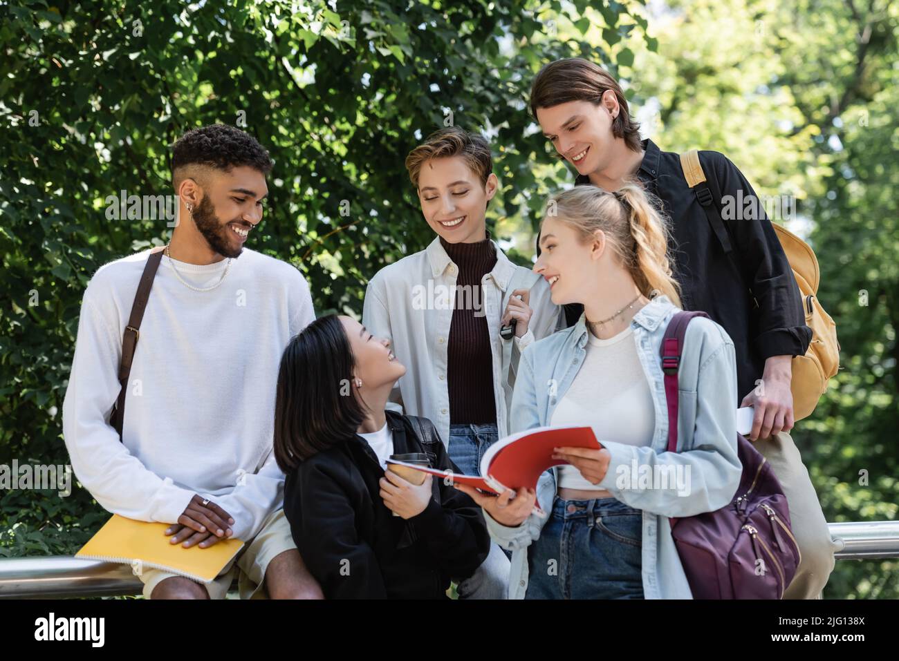 Studente asiatico con takeaway drink parlare con gli amici con notebook nel parco Foto Stock