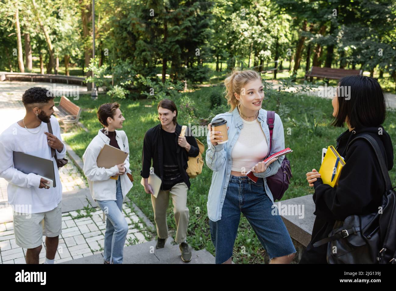 Studenti interrazziali positivi con dispositivi e taccuini che parlano nel parco Foto Stock