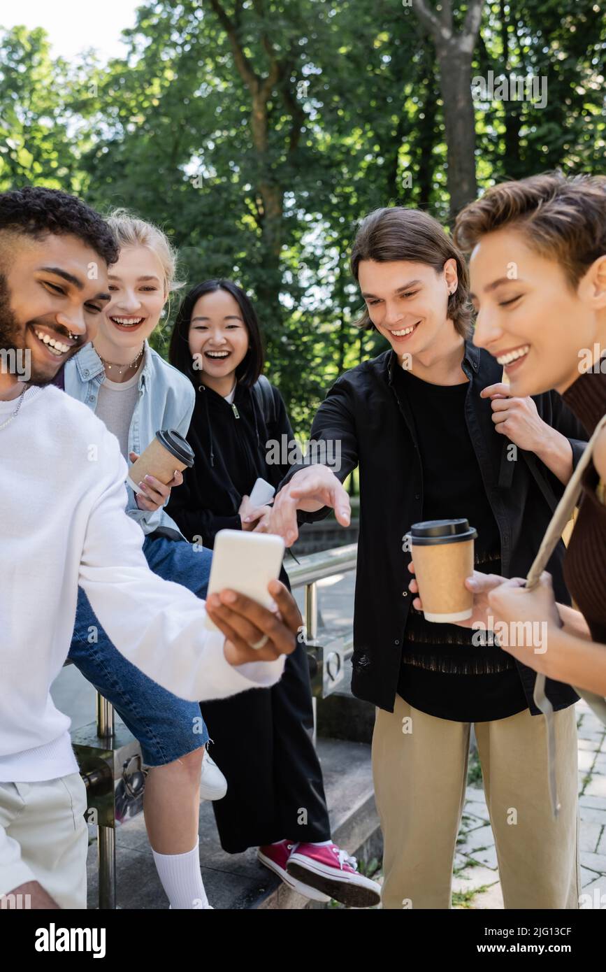 Studenti multietnici con caffè per andare a guardare il cellulare nel parco Foto Stock