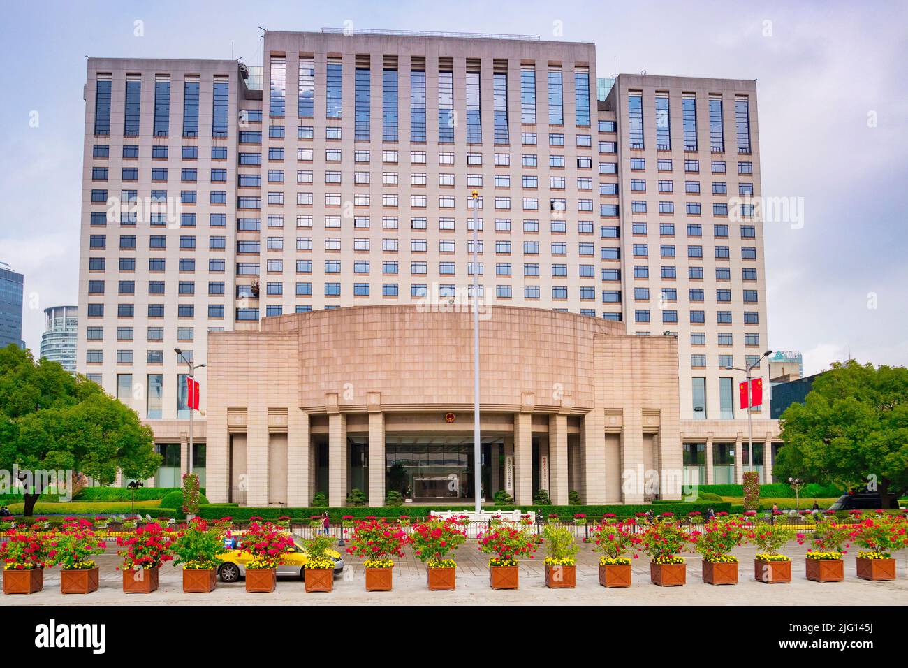2 dicembre 2018: Shanghai, Cina - il Palazzo del Governo del Popolo, di fronte sono vasche di piante e un taxi. Foto Stock