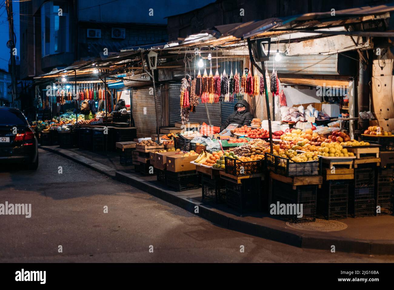 Tbilisi, Georgia - 28 marzo 2022: Vista sul mercato notturno della città di frutta a Tbilisi. Il venditore stanco si è fatto fuori di notte nel mercato. Mercato della frutta e dei dolci Foto Stock