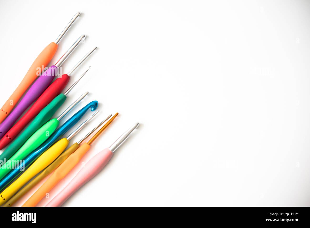 Aghi a crochet luminosi di varie dimensioni isolati su sfondo bianco. Spazio di copia, vista dall'alto. Concetto di idea dell'ago a crochet piatto. Foto Stock