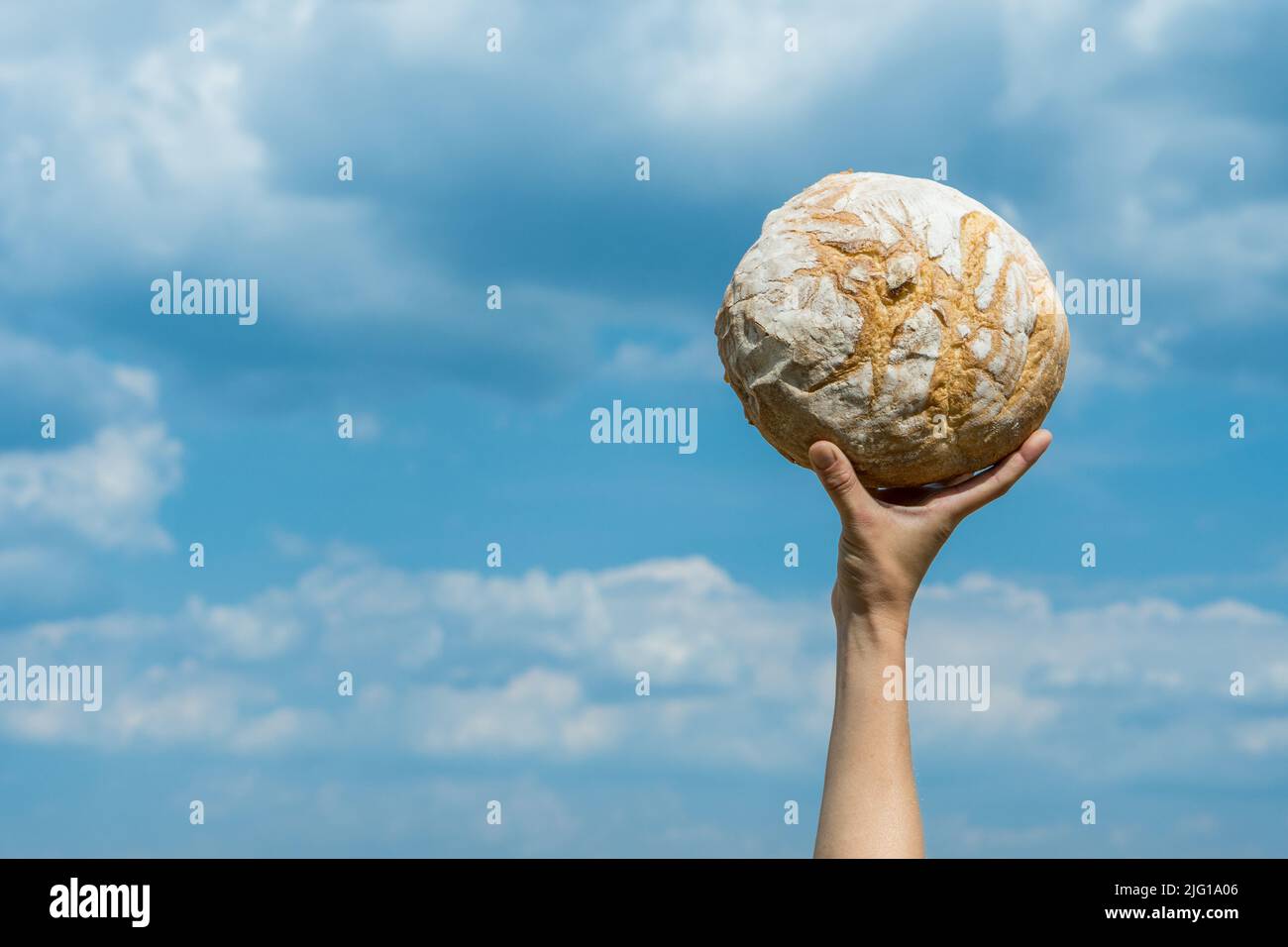 Le mani femminili tengono la pagnotta di pane fatta in casa sopra la sua testa sopra un cielo blu di estate. Concetto di sicurezza alimentare mondiale. Foto Stock