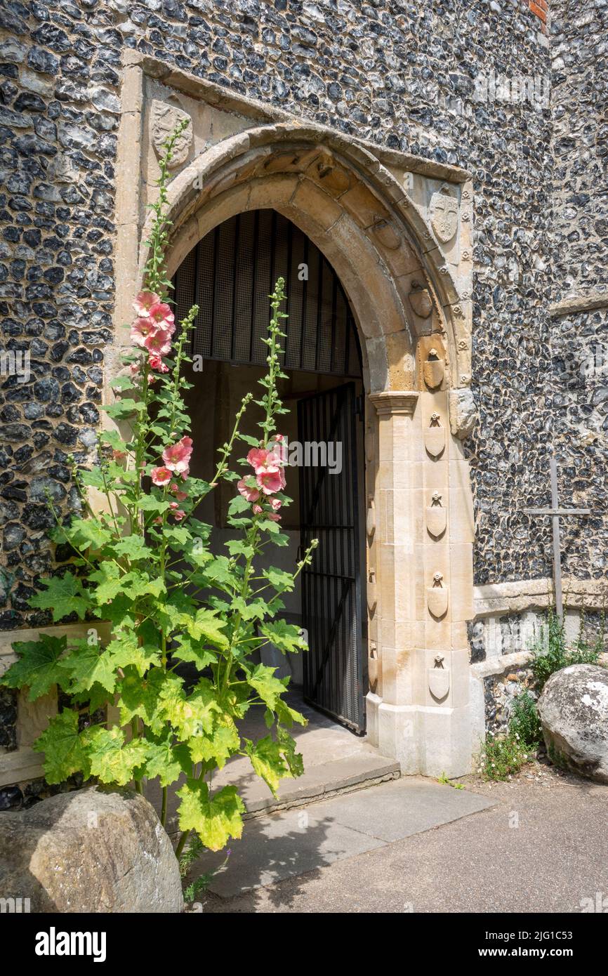 Porta in pietra intagliata circondano con hollyhock vicino a All Saints Church Laxfield, Suffolk Foto Stock