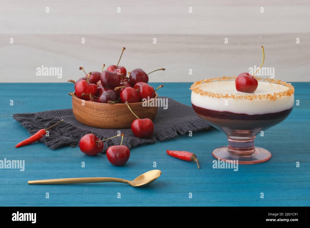 Mousse al cioccolato bianco e scuro o panna cotta con gelatina di ciliegia in un bicchiere con ciotola di legno di ciliegie mature su tavola di legno blu. Vista ad angolo alto, n. Foto Stock