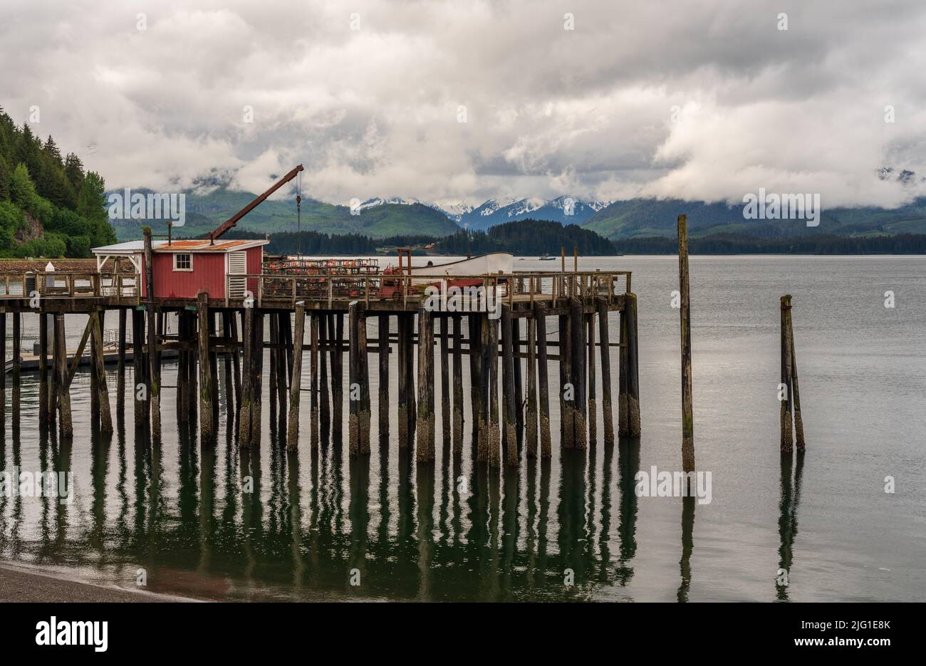 Riflessione del molo di legno nel freddo oceano a Icy Strait Point in Alaska in giorno nuvoloso Foto Stock