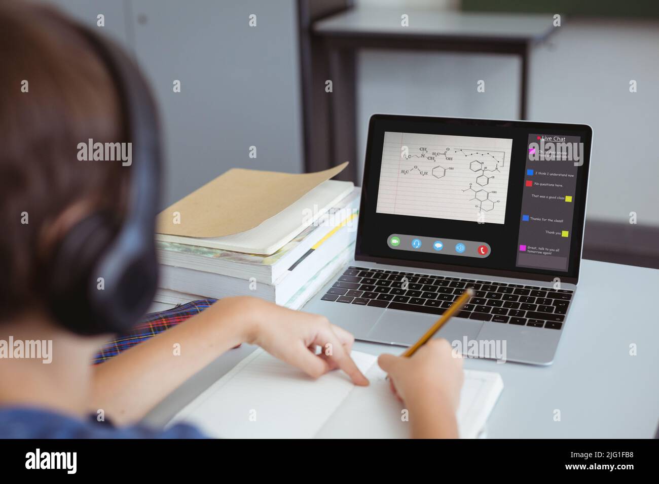 Il ragazzo caucasico scrive le note nel libro mentre osserva lo schermo del laptop durante la lezione in linea nel paese Foto Stock