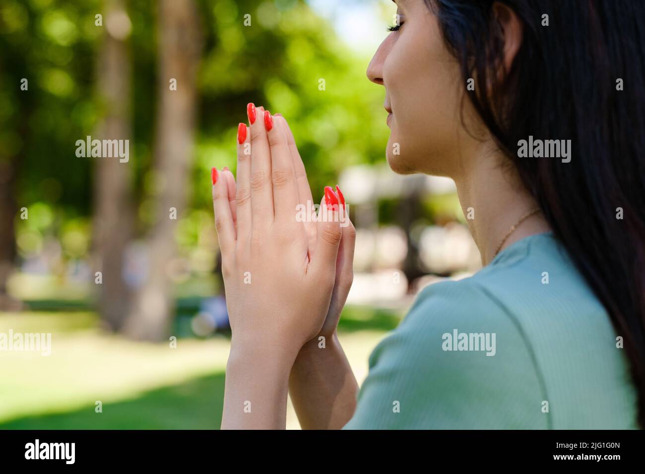 Giovane donna caucasica che indossa tee in piedi sul parco della città, all'aperto tenere le mani in preghiera sentire superstizioso religioso. Dio. Fede, concetto di credenza. Foto Stock