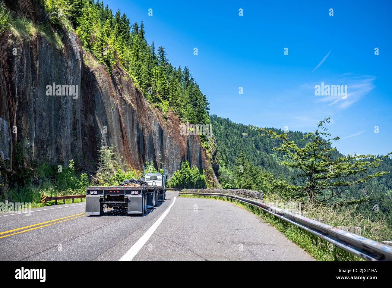 Potente motore nero americano classico grande carro trattore semi-camion con pianale piatto vuoto semi rimorchio guida al magazzino sulla montagna stretta e tortuosa Foto Stock