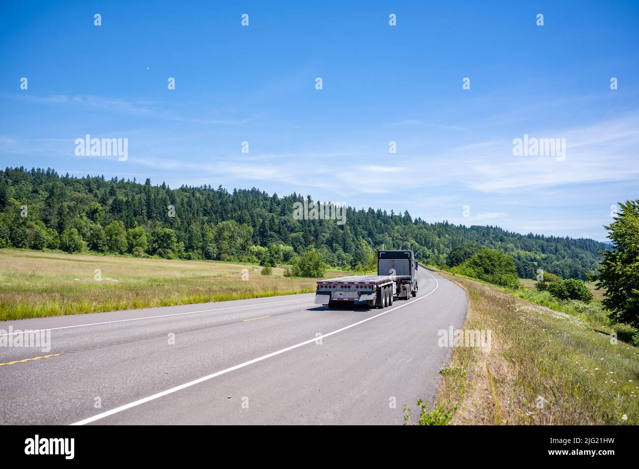 Potente motore nero americano classico grande carro trattore semi-camion con pianale piatto vuoto semi rimorchio guida al magazzino sulla montagna stretta e tortuosa Foto Stock