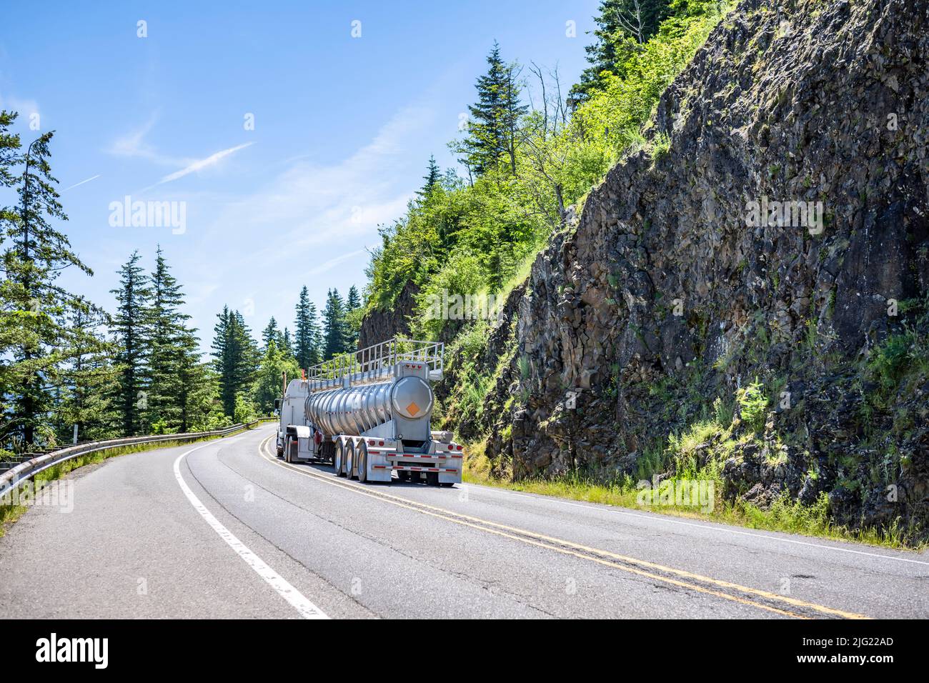 Potente trattore semi-camion bianco con carro grande per il trasporto di carichi in concime conico semi-rimorchio sfusi che guida su tortuose strade di montagna con pareti rocciose Foto Stock