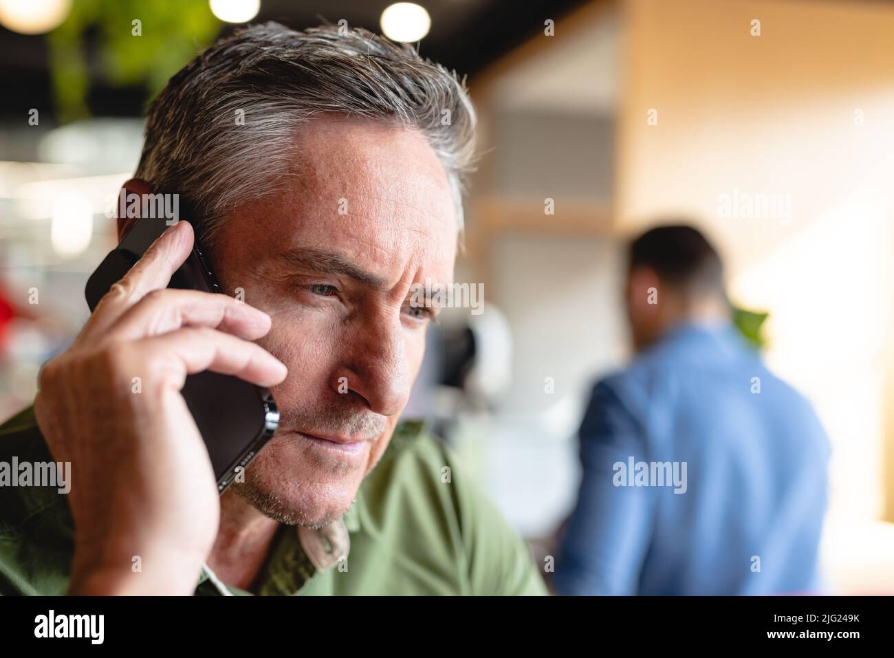 Primo piano di un uomo d'affari maturo che parla su smartphone in ufficio creativo Foto Stock