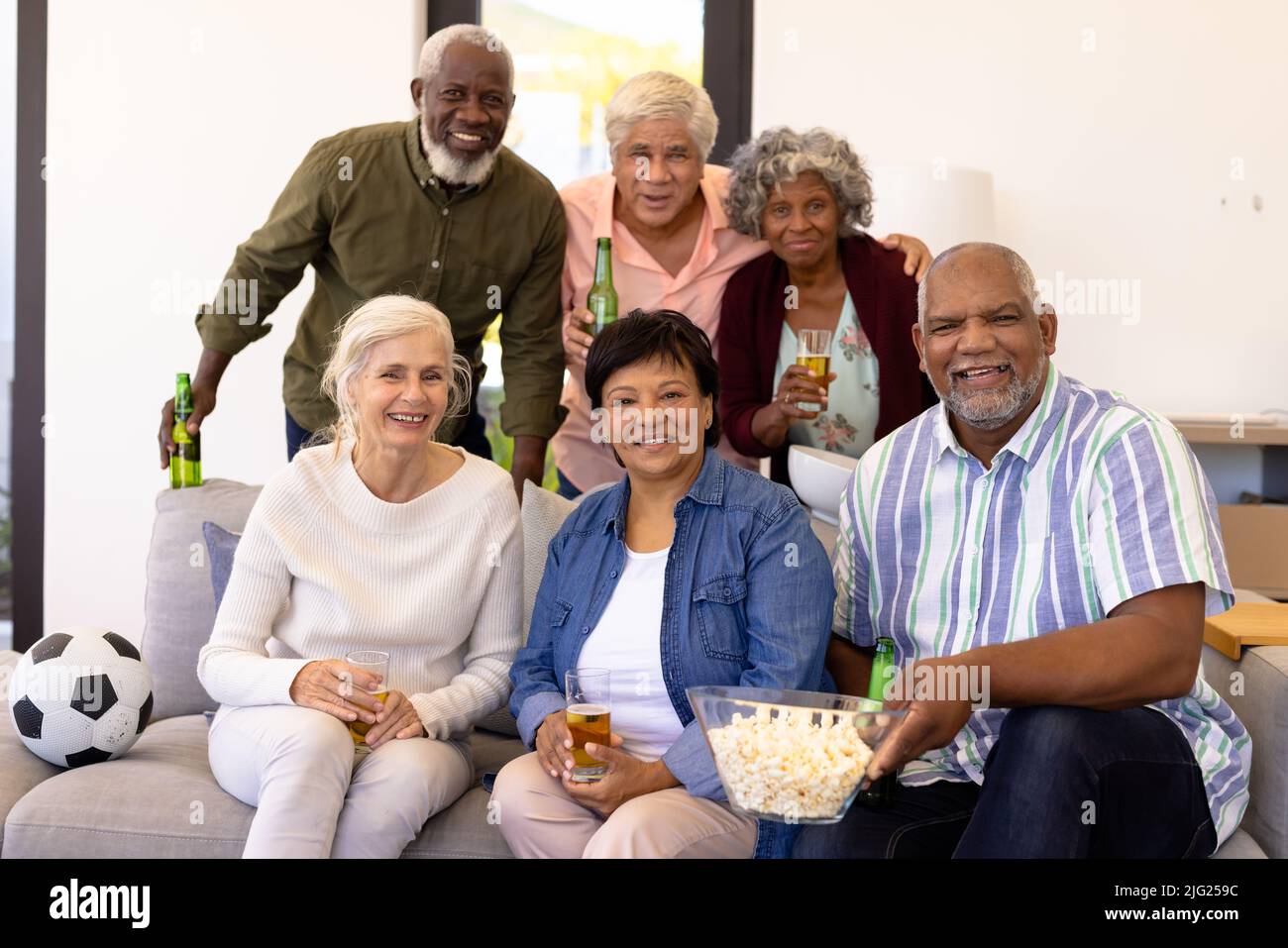 Ritratto di allegri amici anziani multirazziali con birra e popcorn godendo partita in casa di cura Foto Stock