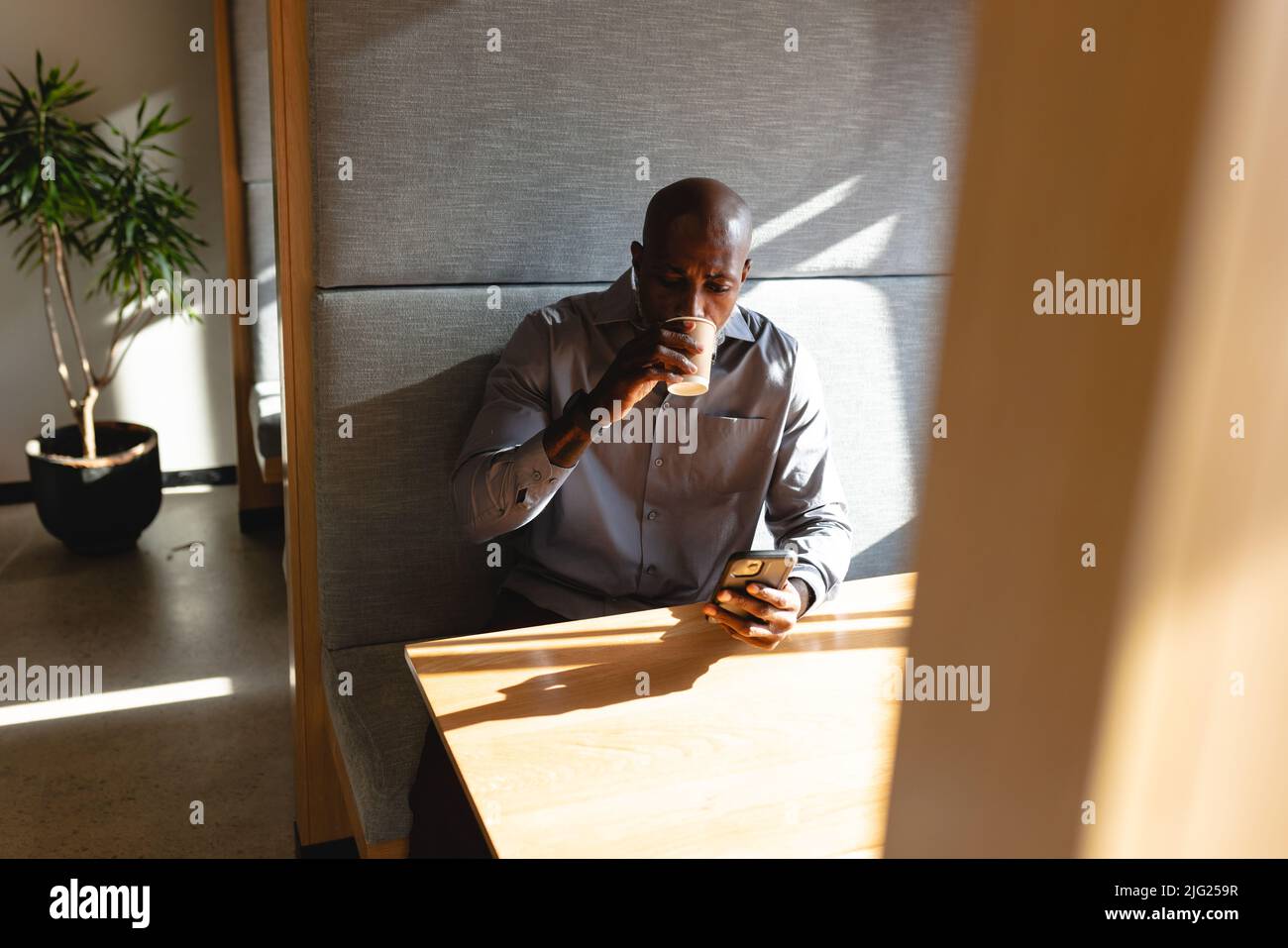 Uomo d'affari africano americano maturo usando lo smart phone mentre ha il caffè durante la pausa in ufficio Foto Stock